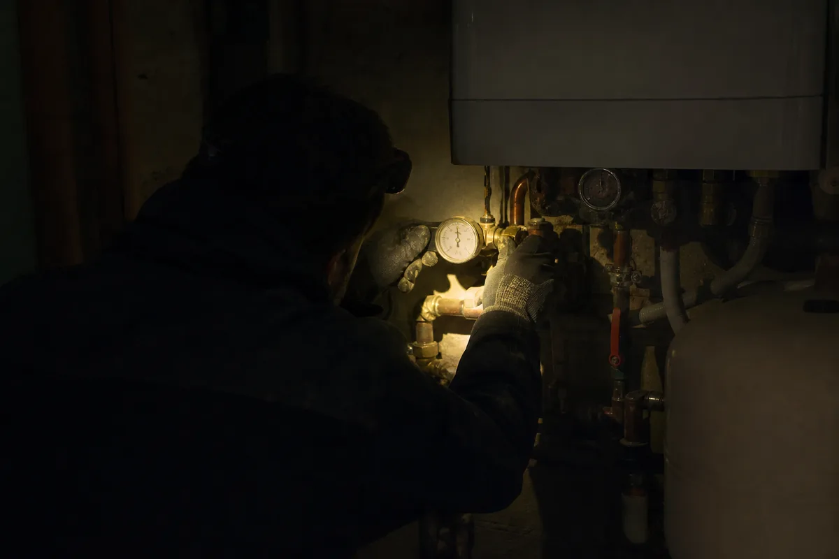 Technicien de dos vérifiant un manomètre de chaudière à la lampe frontale, ambiance nocturne